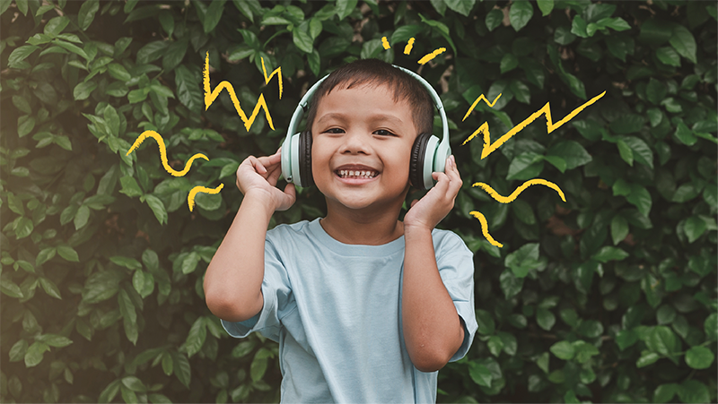 Little boy in front of greenery listening to headphones